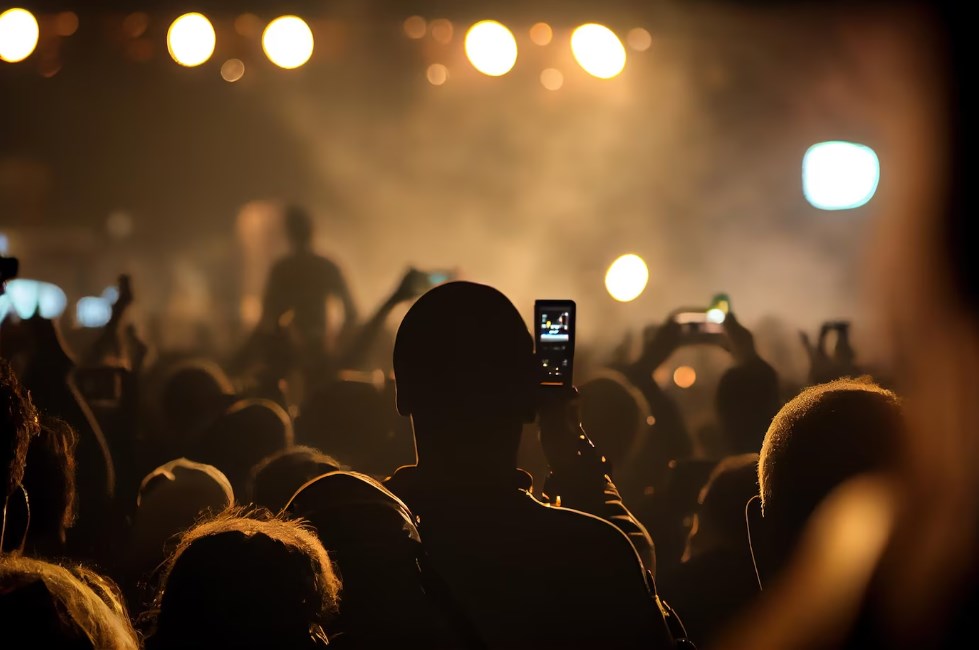 back view of a crowd of fans watching and filming a live concert performance