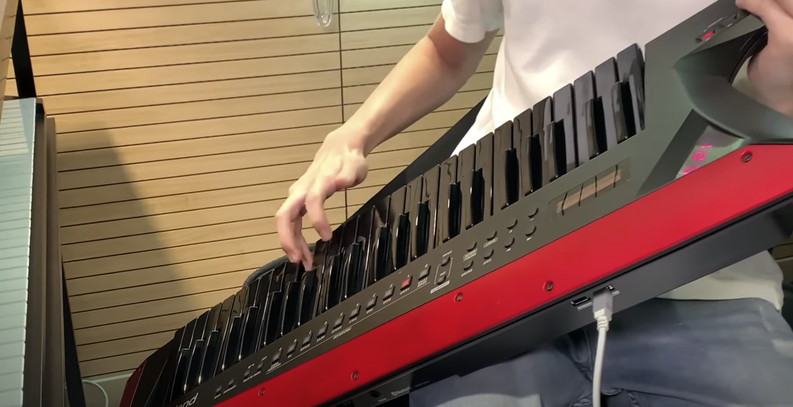 Photo of a guy dressed in white holding a red and black Roland AX-Edge Keytar