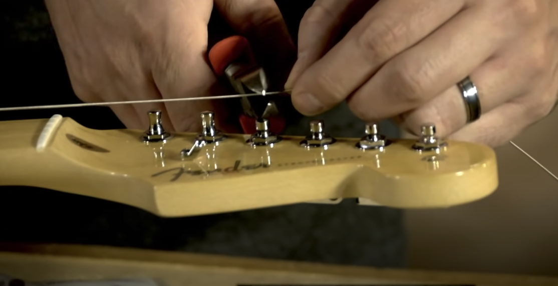 Photo of a hand holding a guitar string, while the other hand holds a wire-cutting tool