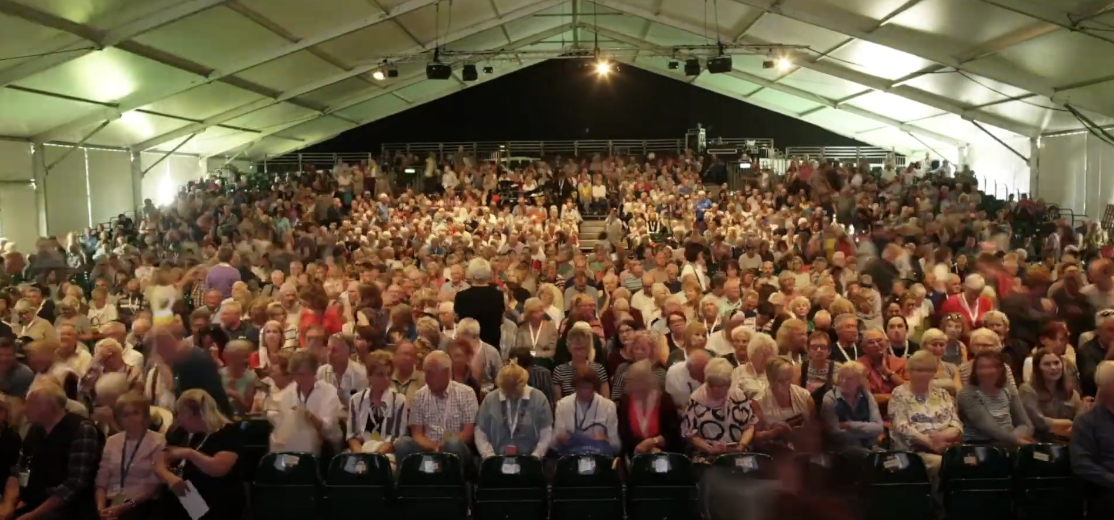 Photo of a large group of people gathered and seated together in a covered area