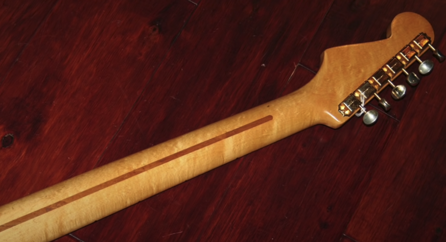 Photo of the neck of a Fender Stratocaster guitar displayed against a wooden red background