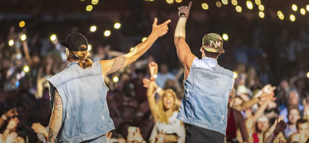 Photo of two guys singing on stage, with a large crowd of people watching her concert