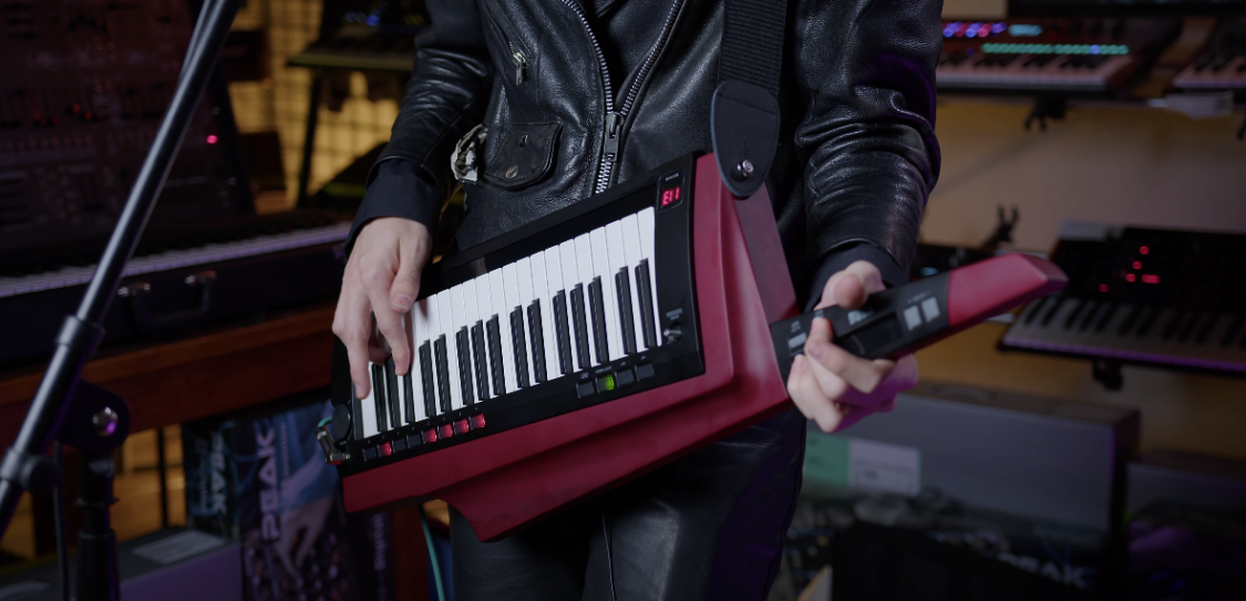 Photo of a person dressed in black leather jacket holding a maroon Korg RK-100S Keytar