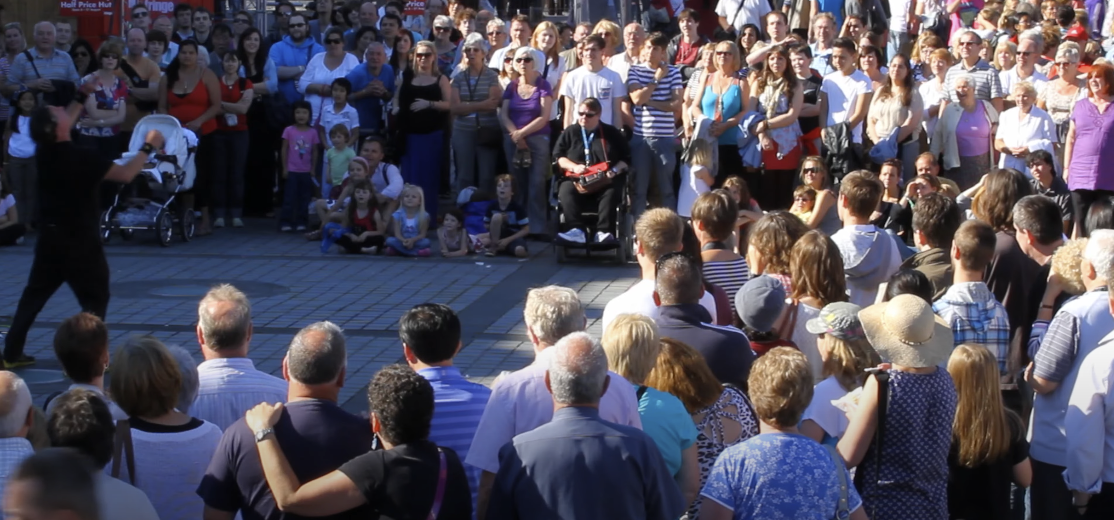 Photo of a large crowd gathered in a circle, attentively watching a performer in the center