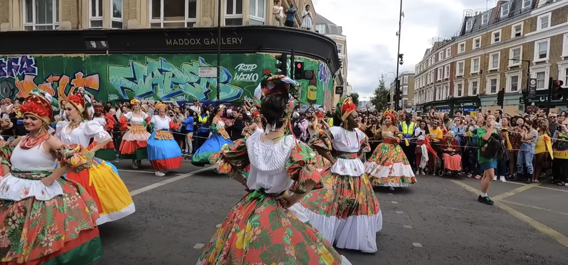 Photo of females in colorful costumes dancing in the middle of the road