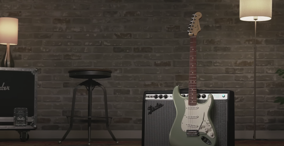 Green guitar in front of a big amplifier, with a chair and lamp nearby