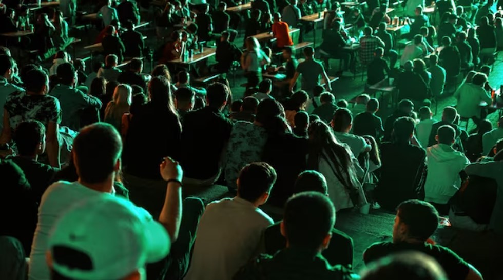 a crowd of people sitting and watching a live show in a public place at night